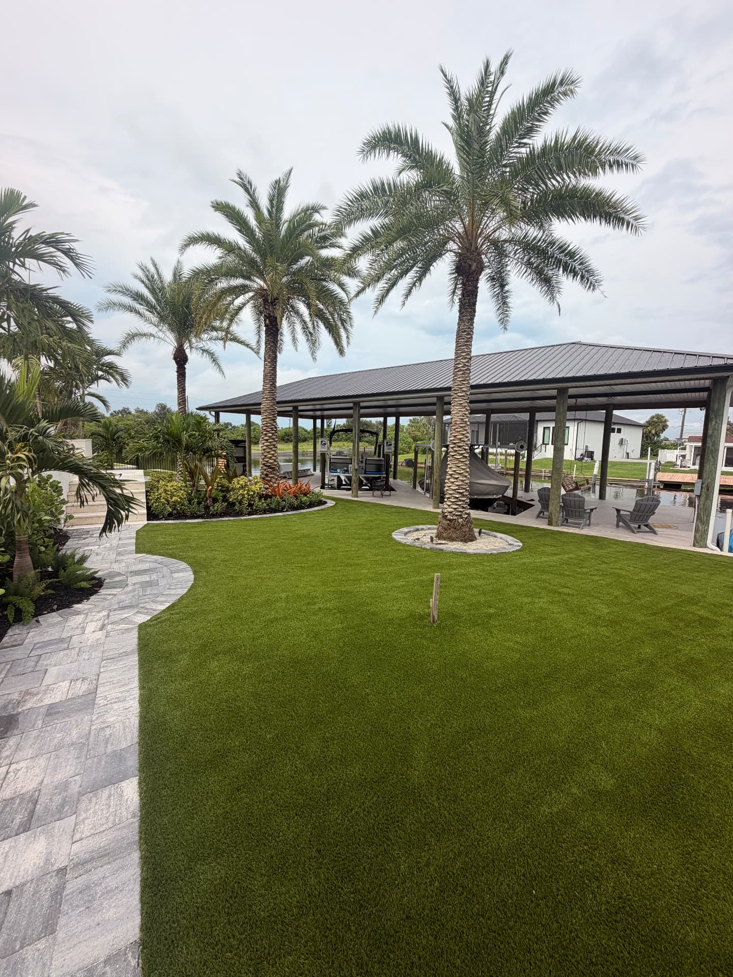 Artificial turf lawn with date palms and paver walkway at a waterfront home