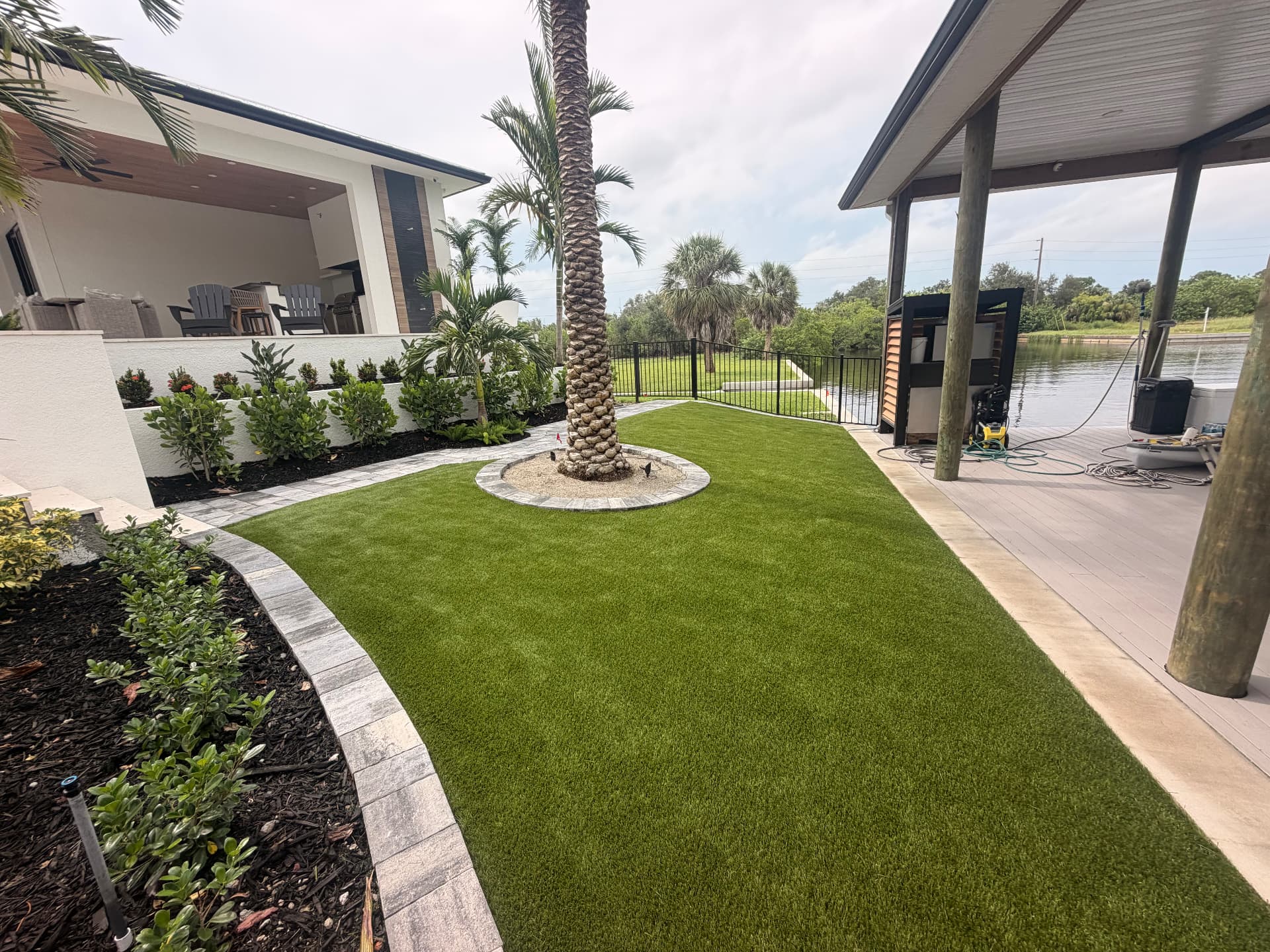 Canal-front artificial turf lawn with paver edging and tropical beds